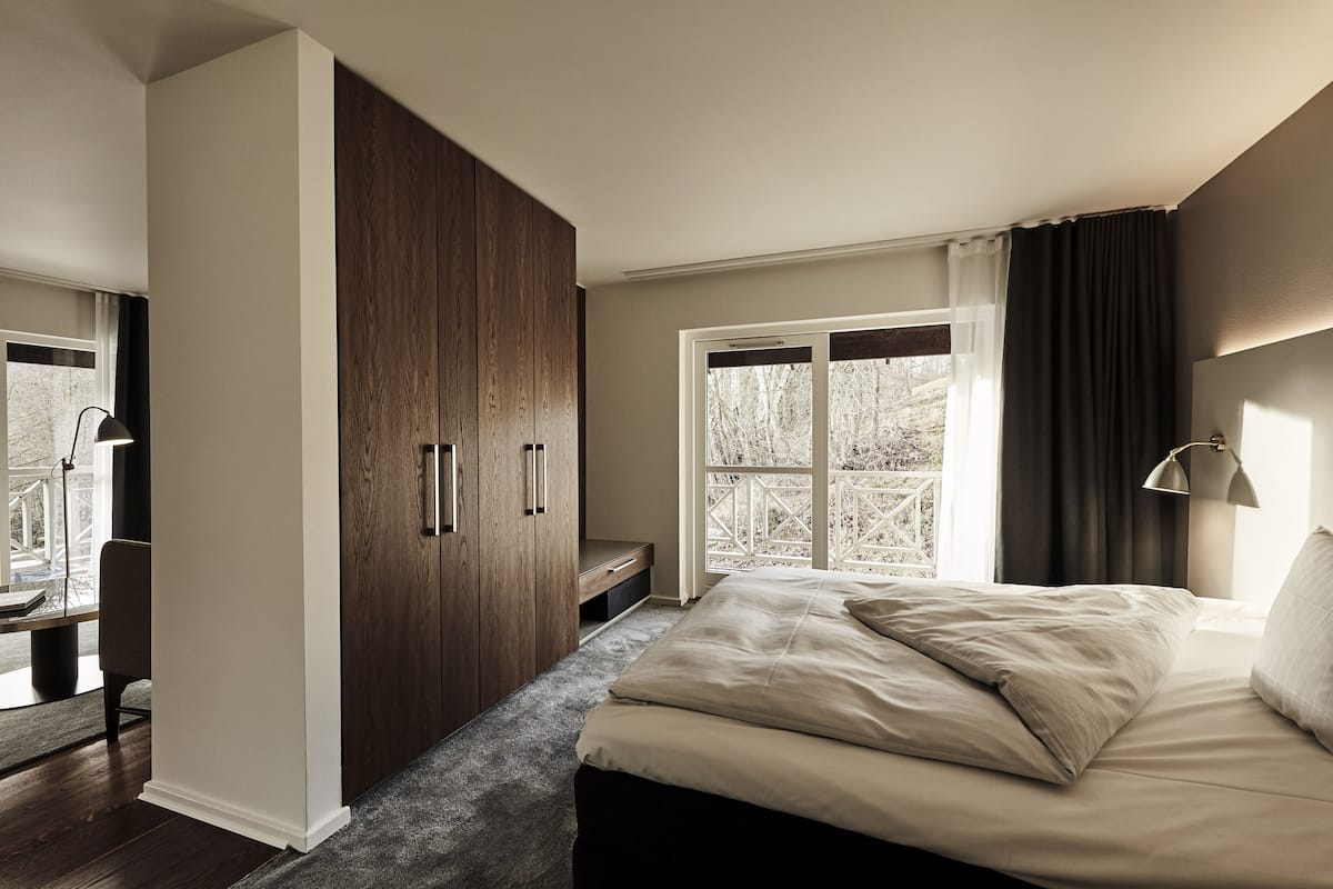 A bedroom with a bed, a wardrobe, a desk, and a window with curtains.