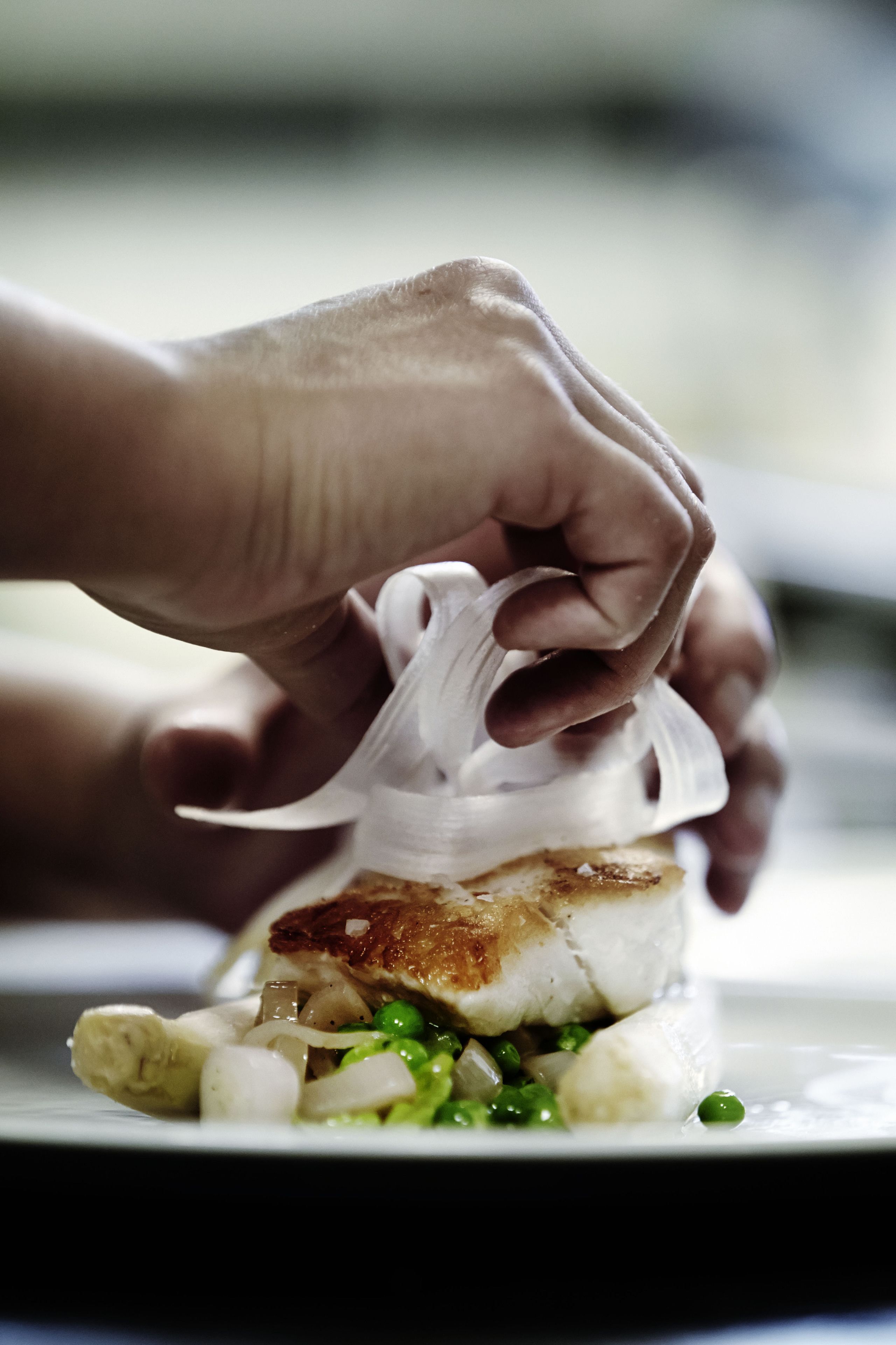 Primer plano de manos preparando un plato con pescado, guisantes y cebollas.