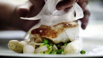 Primer plano de manos preparando un plato con pescado, guisantes y cebollas.