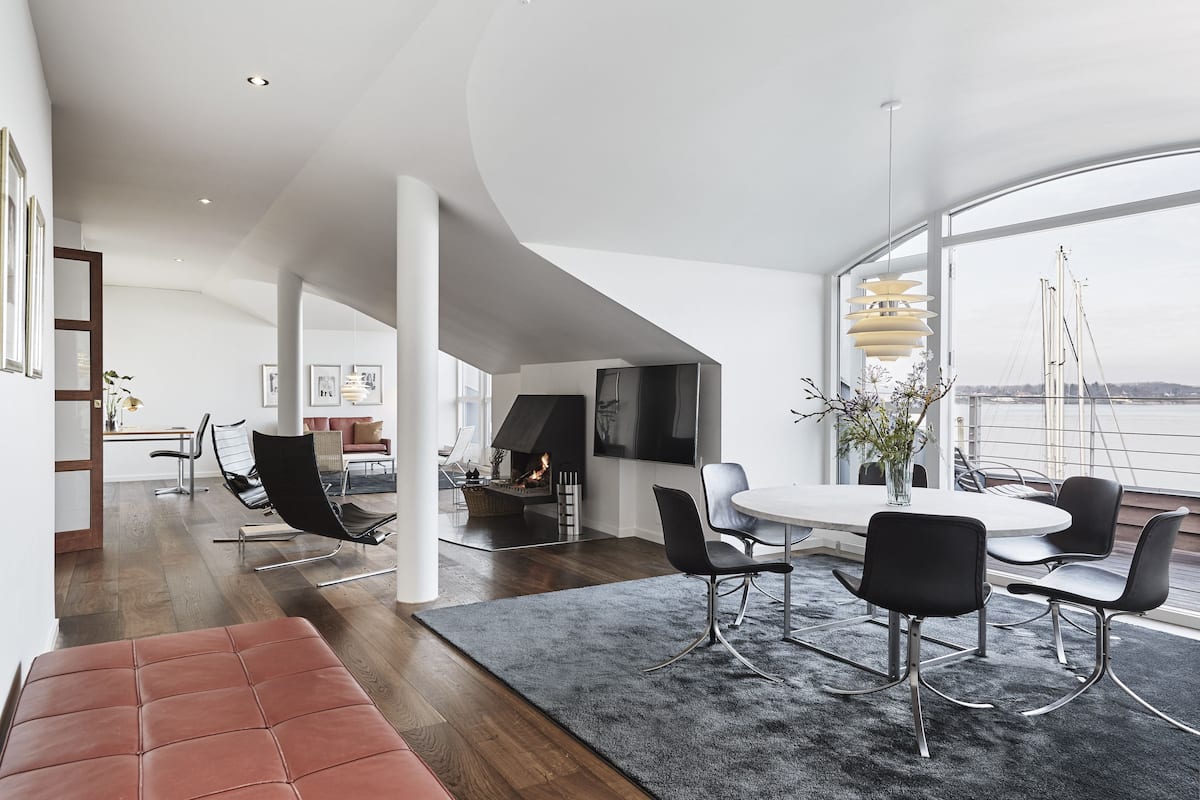 A modern living room with a fireplace, a dining area with a round table and chairs, and large windows offering a view of the city.