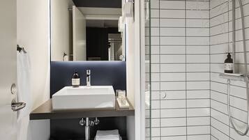 Un baño moderno con ducha envuelta en vidrio, un lavamanos blanco y piso oscuro.