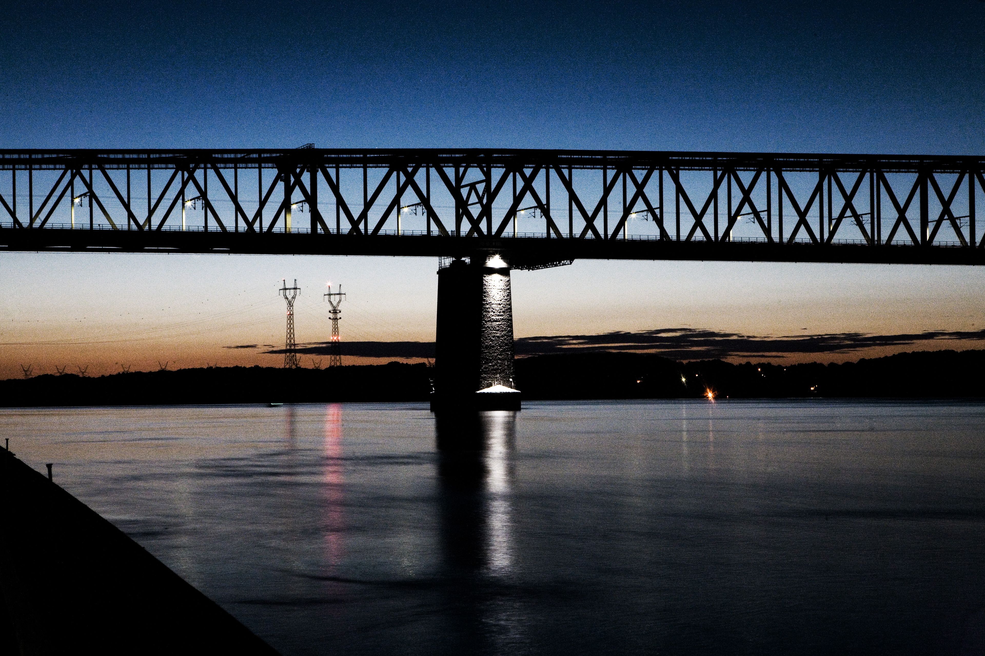 Een nachtzicht van een brug over een rustig waterlichaam, met een silhouet van een toren op de achtergrond.