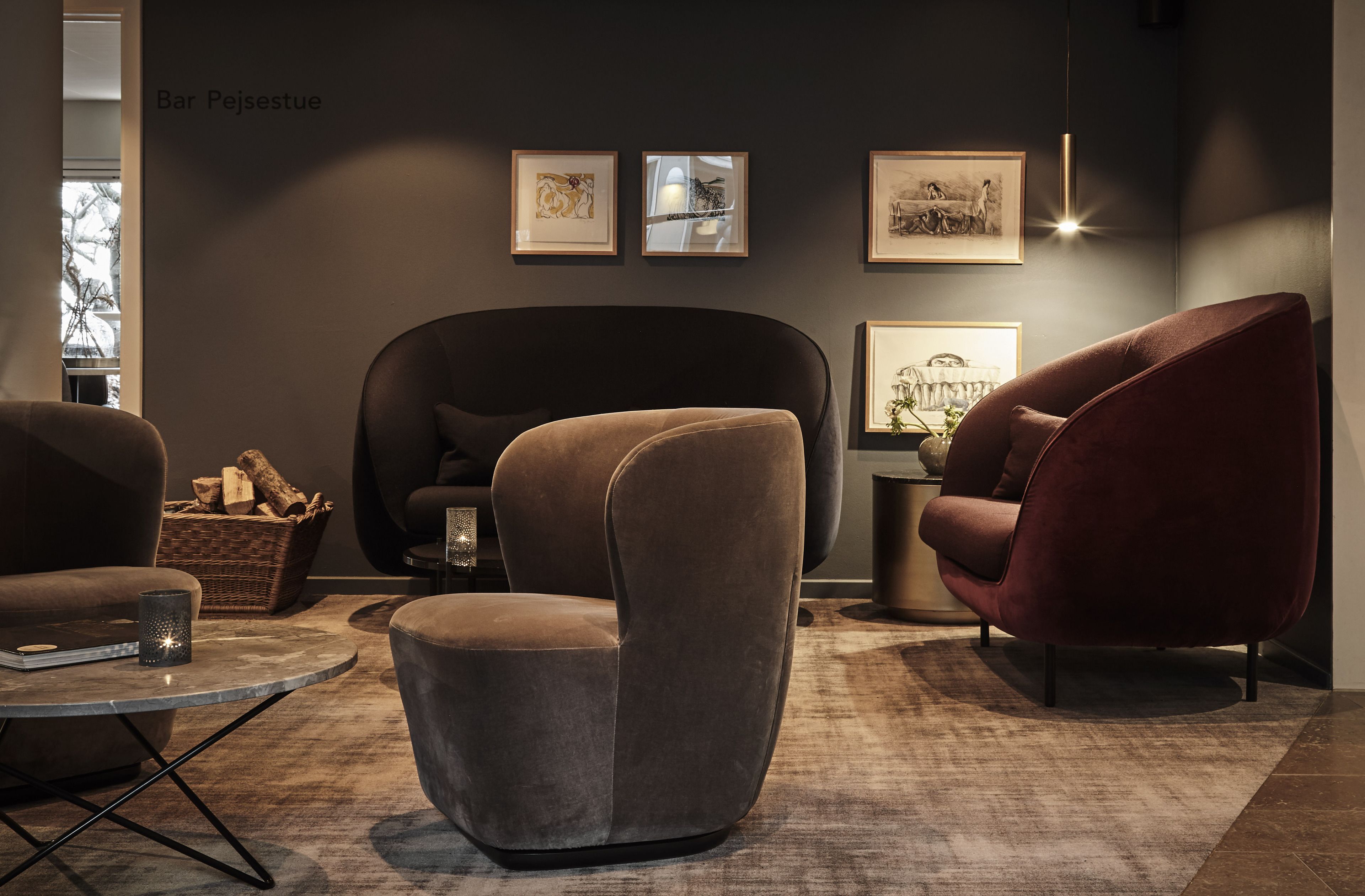 A modern living room with a dark wall, three framed artworks, and two plush armchairs.