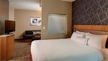 A hotel room with a large bed, a desk with a flat-screen TV, a sofa, and a framed picture on the wall.