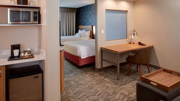 Habitación de hotel con cama, escritorio, silla, microondas, cafetera y refrigerador pequeño.