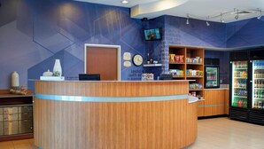 A reception area with a wooden reception desk, a clock, a television mounted on the wall, and a refrigerator stocked with beverages. - SpringHill Suites St. Louis Brentwood (Brentwood)
