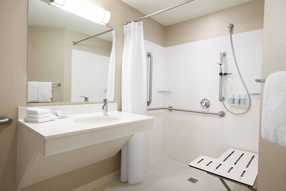 A modern bathroom with a large sink, mirror, shower, and grab bars.