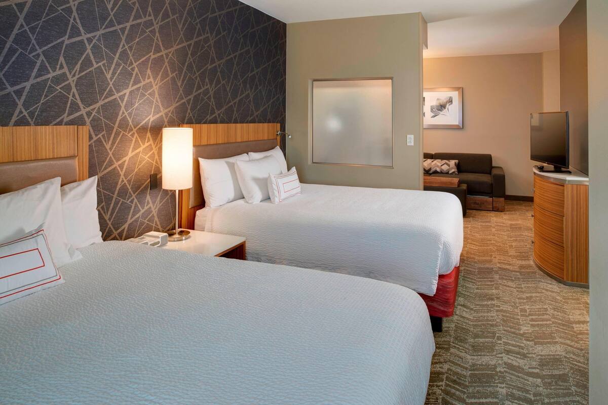 A hotel room with two beds, a TV, a desk, and a sofa.