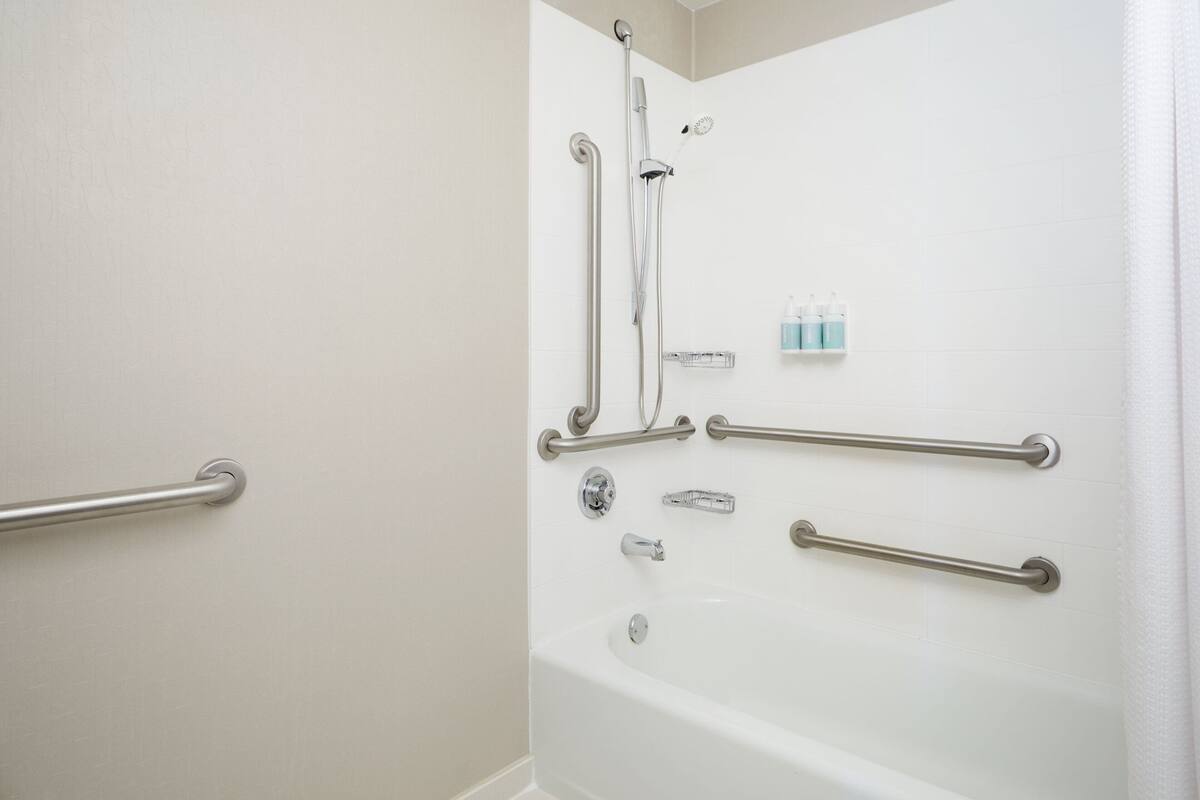 A bathroom with a bathtub, grab bars, and a showerhead.