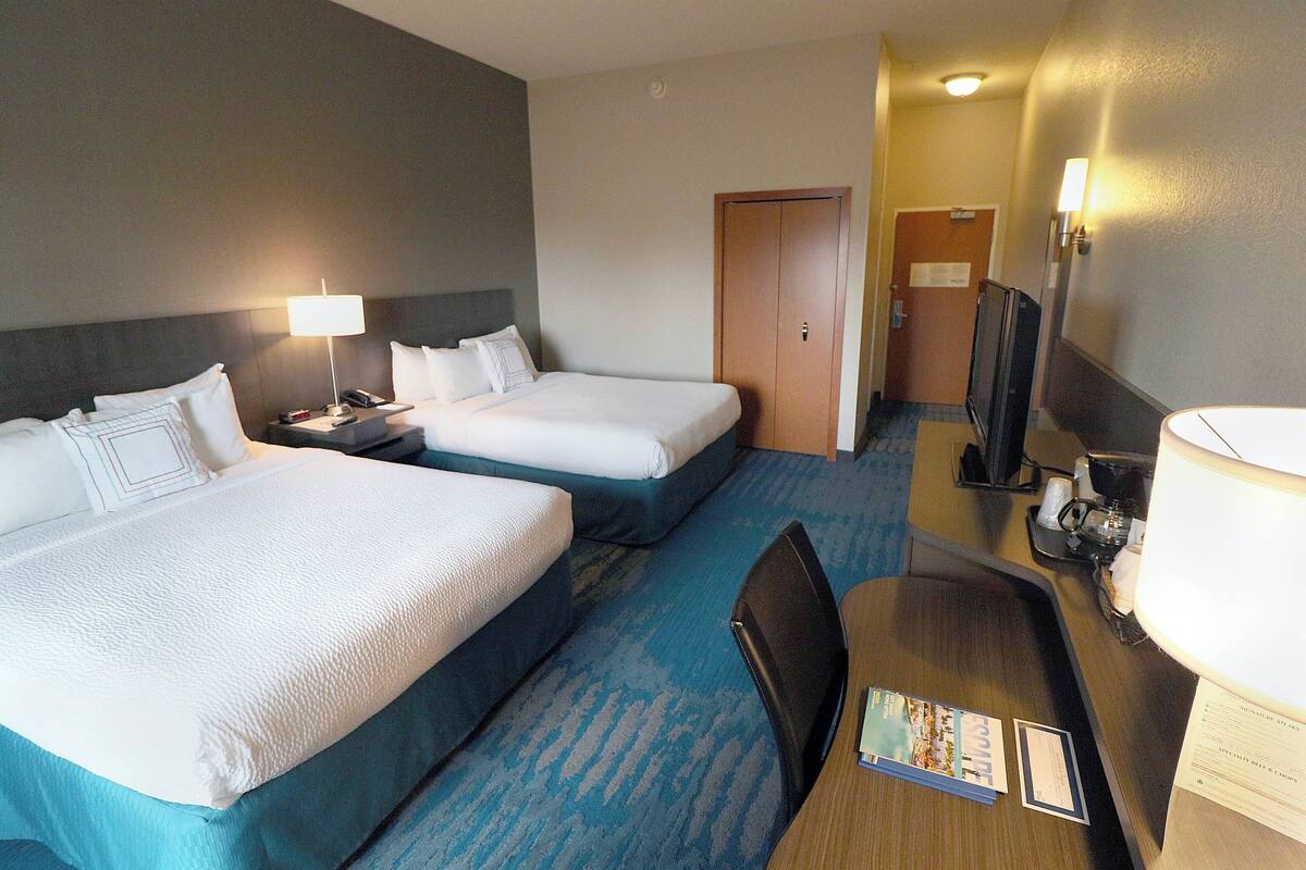 Une chambre d’hôtel avec deux lits, un bureau, une chaise, une télévision et une lampe.