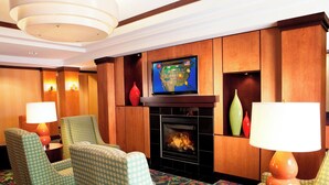 Eine Hotellobby mit Kamin, grün gemusterten Sesseln, einem Fernseher über dem Kamin und einem gemusterten Teppich.
