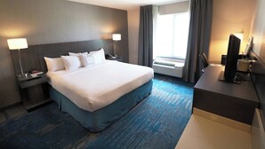 Ein Hotelzimmer mit einem großen Bett, einem Schreibtisch, einem Fernseher und einem Fenster mit Vorhängen.