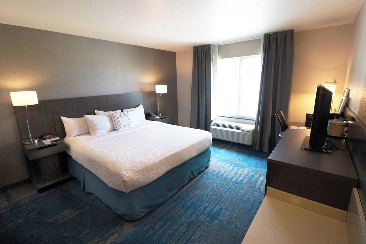 Une chambre d’hôtel avec un grand lit, un bureau, une télévision et une fenêtre avec des rideaux.