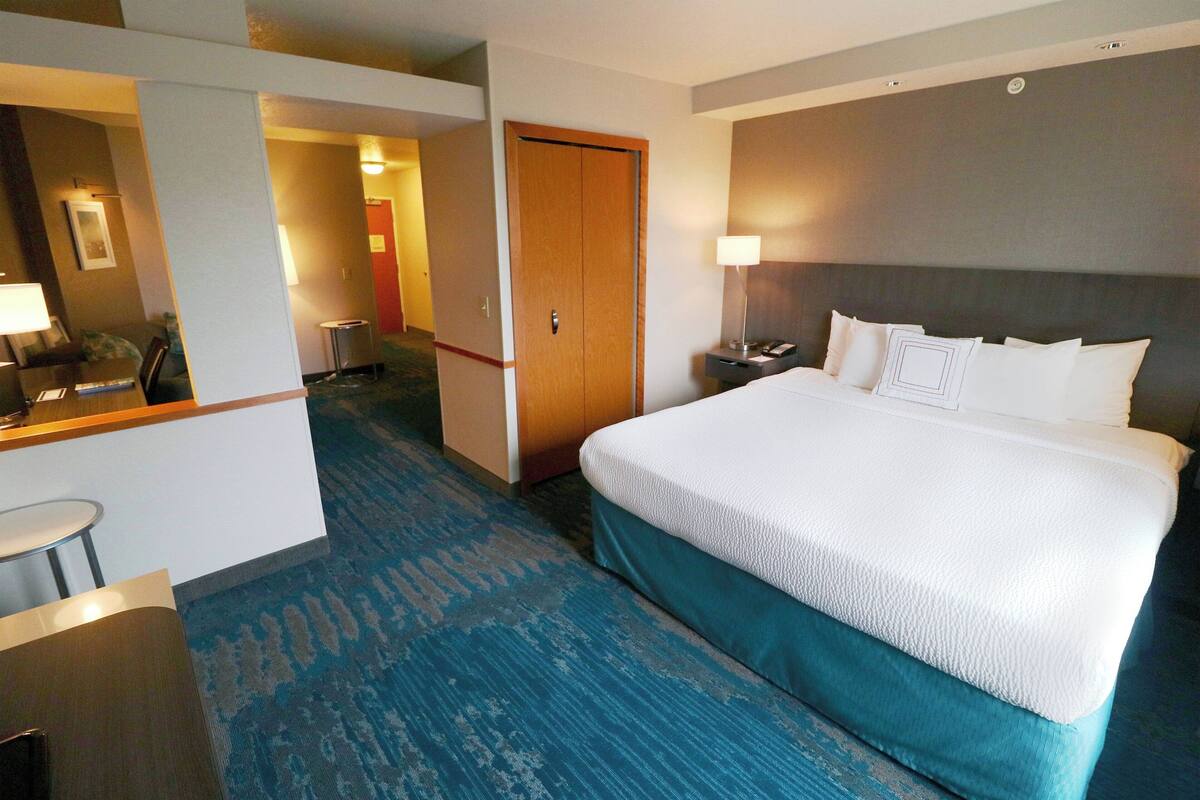 Une chambre d’hôtel avec un grand lit, un bureau avec une chaise, une lampe et une porte donnant sur une autre pièce.