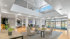 A spacious lobby with a high ceiling, a reception desk, seating area, and a view of the parking lot through glass doors. - Holiday Inn Express Leigh - Sports Village by IHG (Leigh)