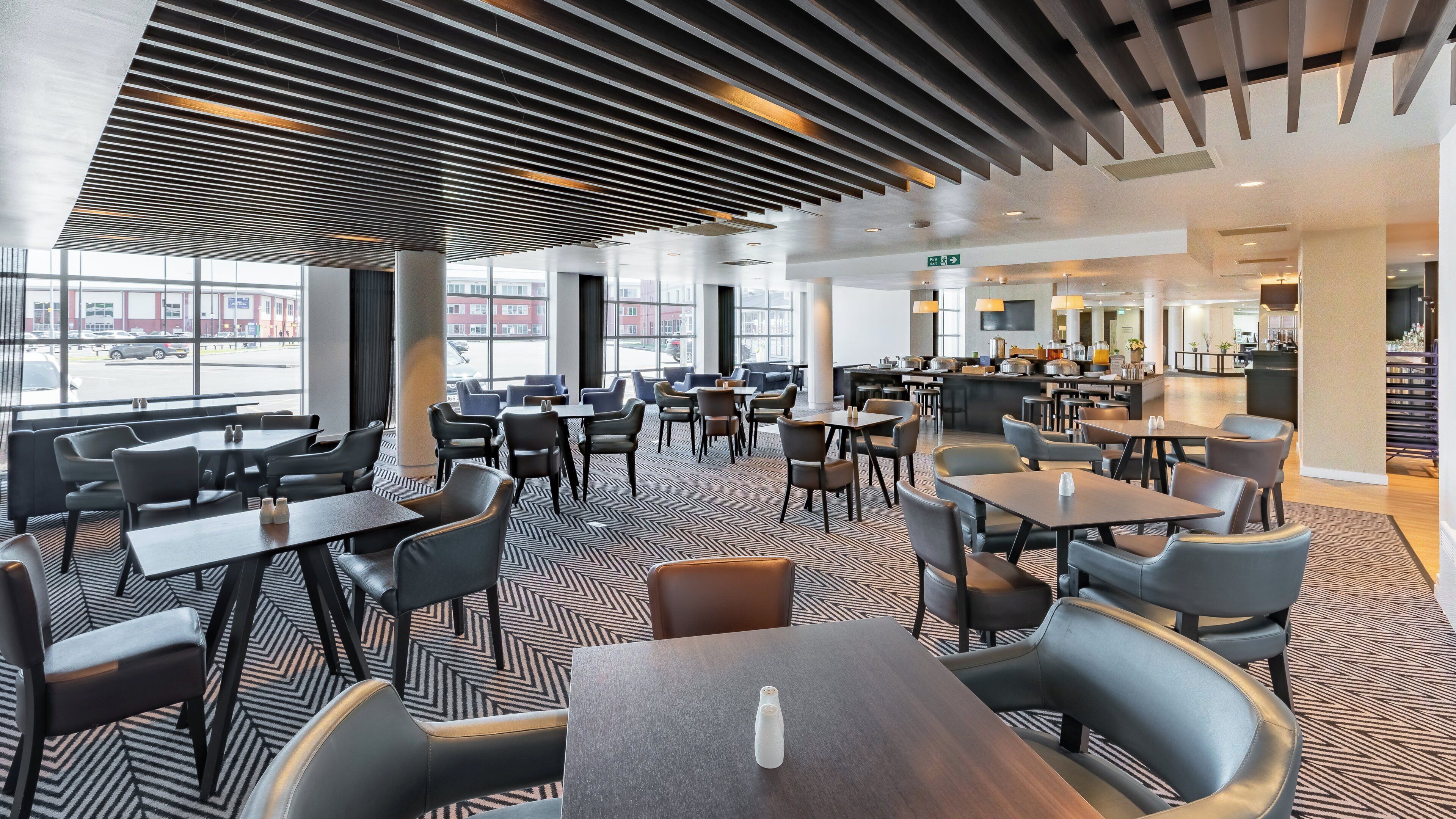 A modern restaurant with a central bar area, multiple seating options, and large windows offering a view of the street.
