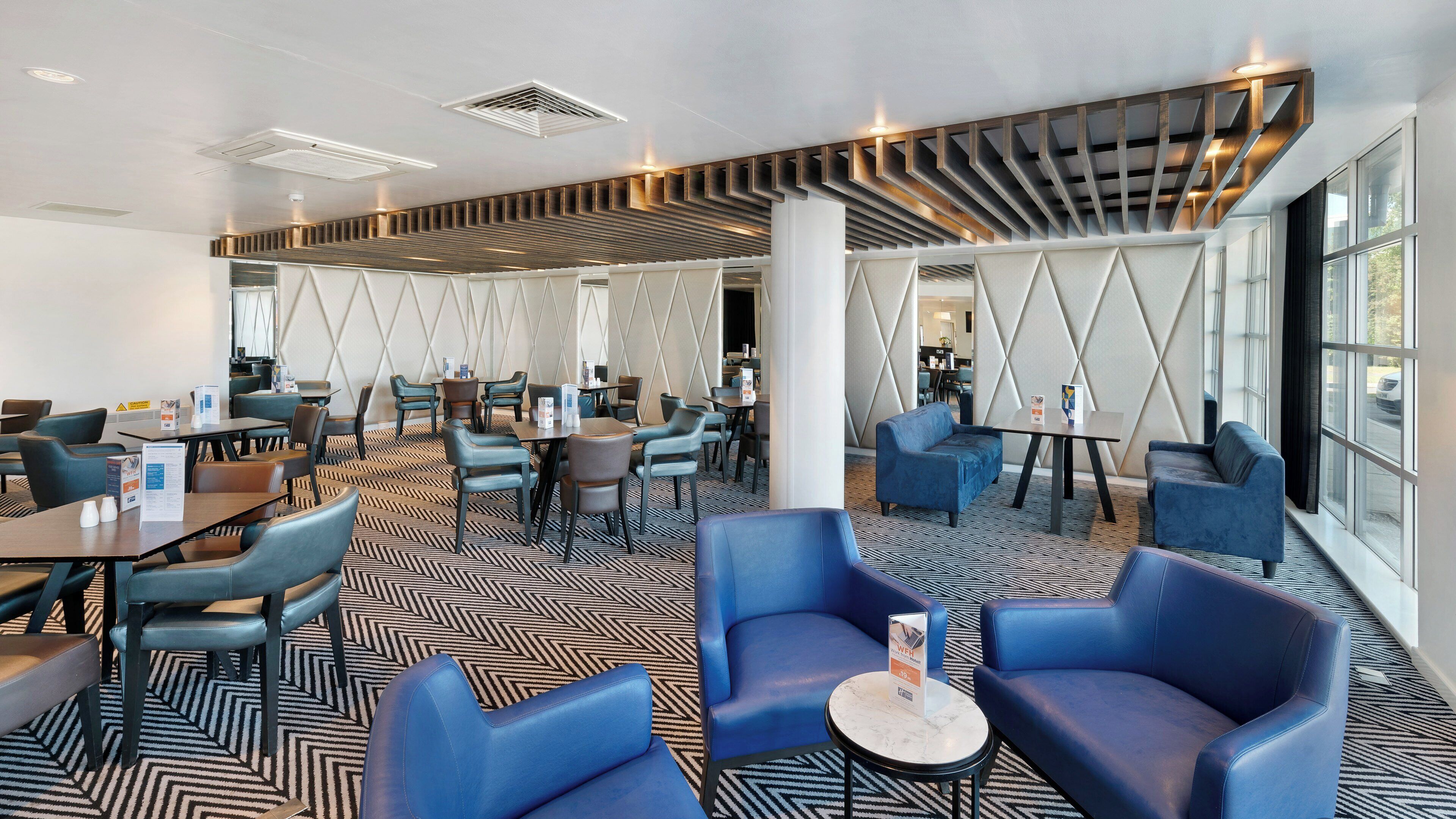 Un moderno vestíbulo de hotel con alfombra de diseño geométrico, asientos azules y una decoración contemporánea.
