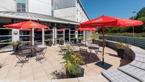 An outdoor patio area with red umbrellas, seating arrangements, and potted plants. - Holiday Inn Express Leigh - Sports Village by IHG (Leigh)