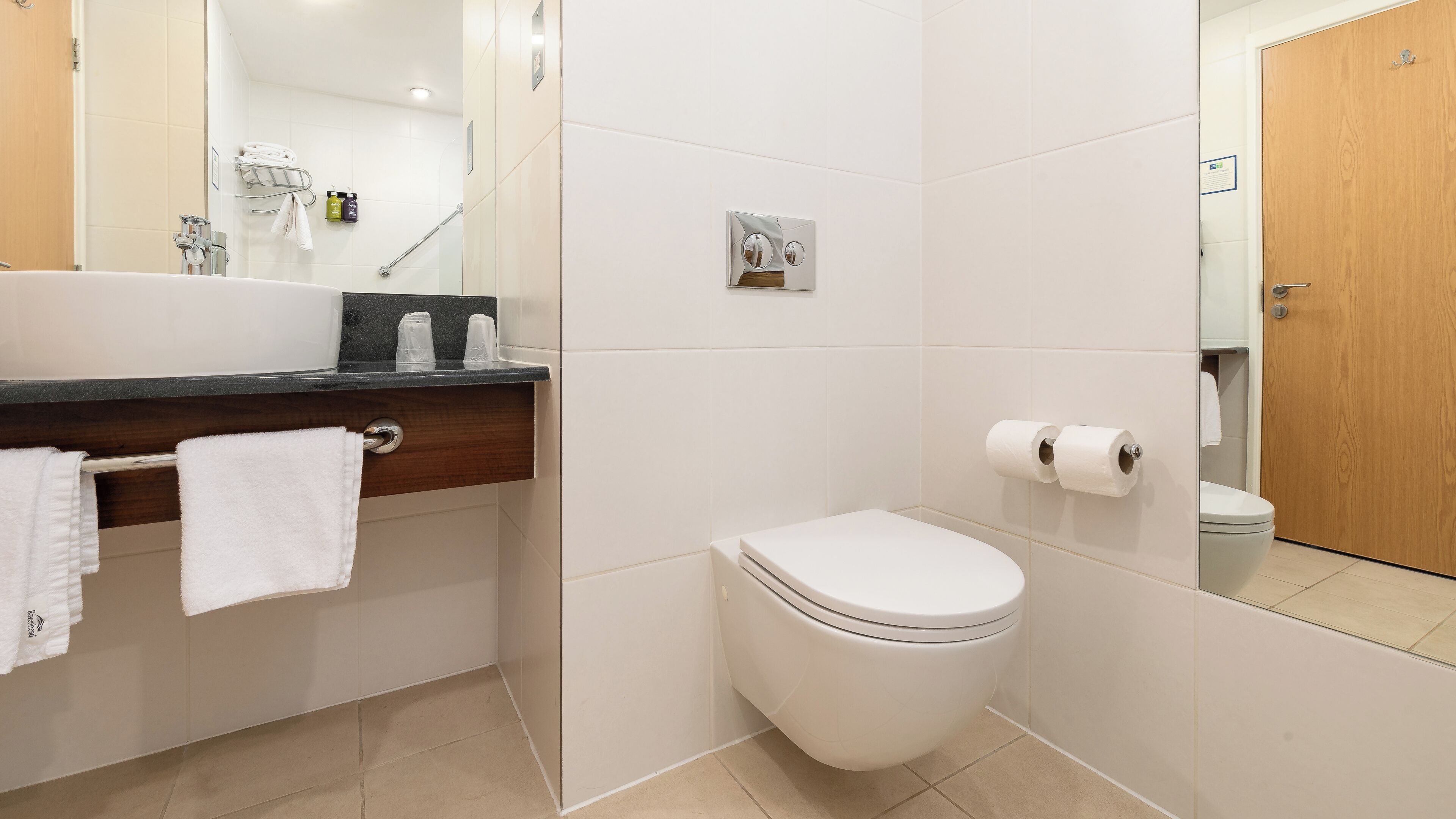 Un baño moderno con inodoro blanco, lavabo con espejo y toallero.