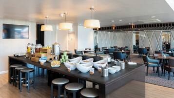 A modern hotel lobby with a central bar area, seating arrangements, and a large screen.