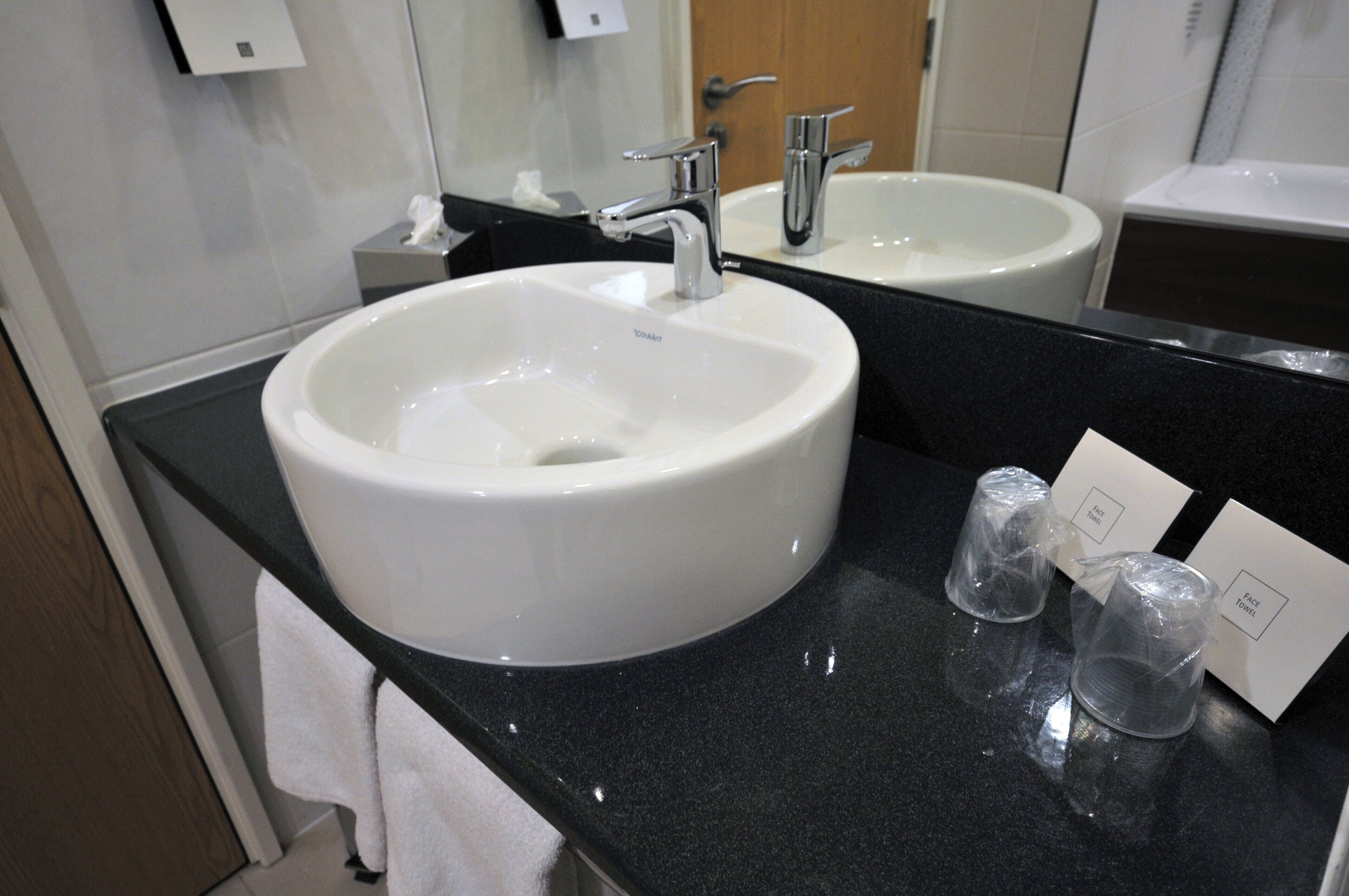 A bathroom with a white sink, a mirror, and a black countertop.