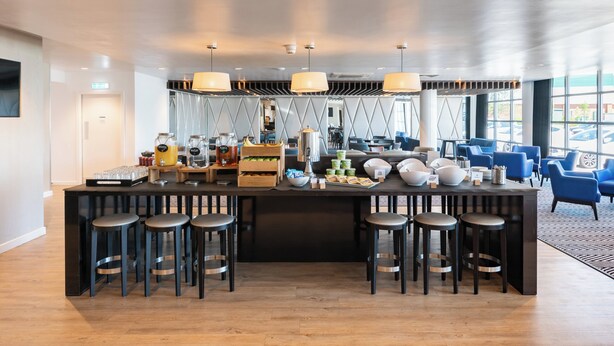 A modern bar area with a central island, bar stools, and a variety of beverages and snacks. - Holiday Inn Express Leigh - Sports Village by IHG (Leigh)