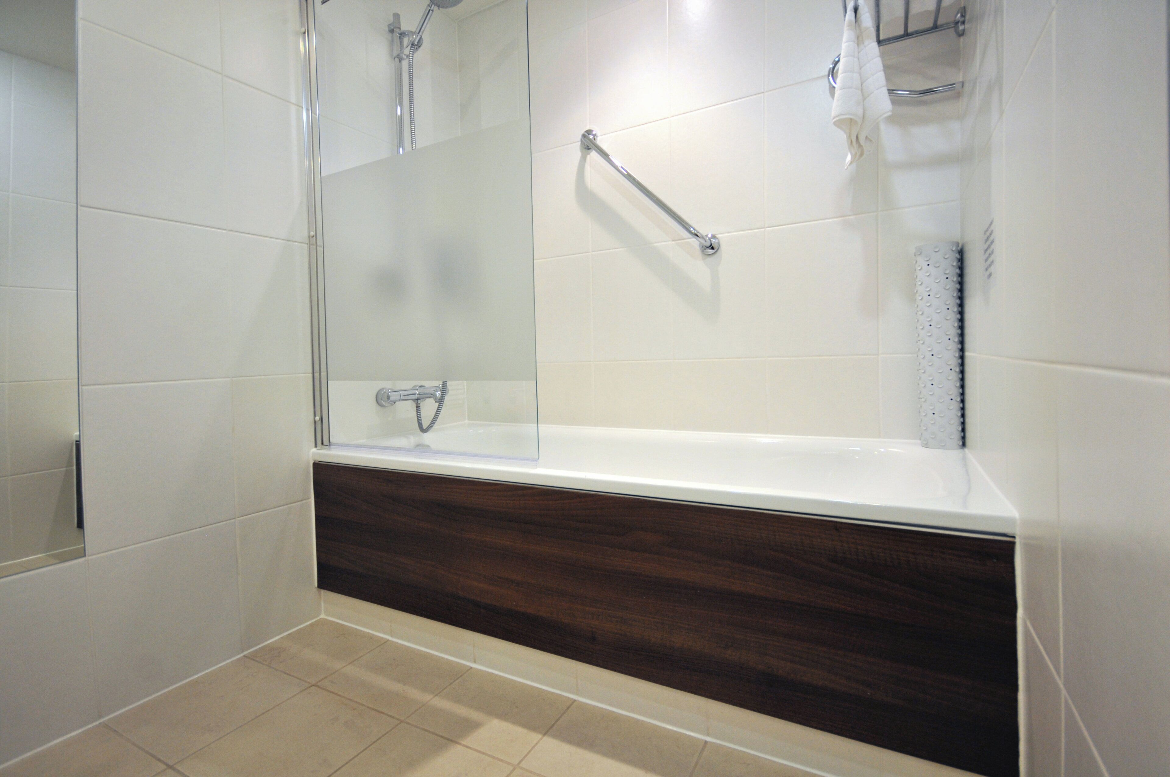 A modern bathroom with a glass-enclosed shower, a wooden vanity, and a white tiled floor.