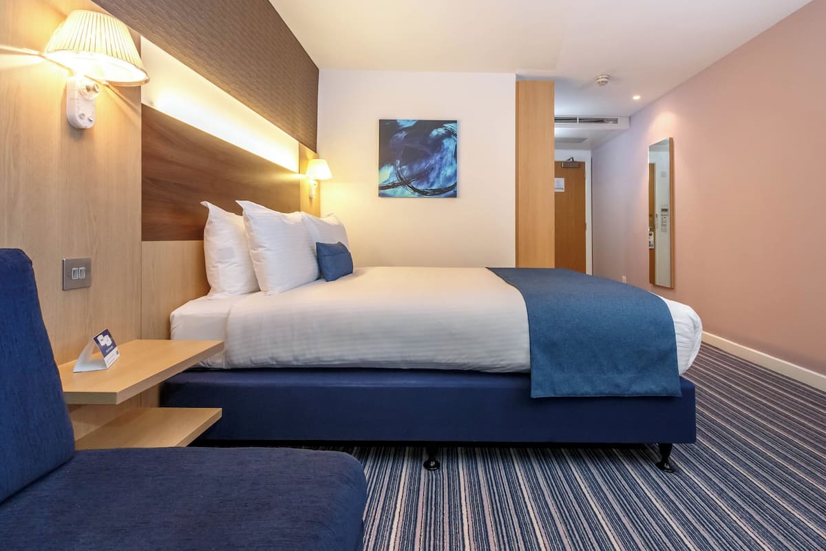 A hotel room with a large bed, bedside lamps, a small table, and a blue chair.