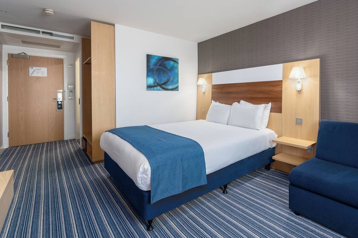 A hotel room with a large bed, a blue sofa, a painting on the wall, and a wooden headboard.