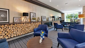 A modern lobby with a fireplace, blue seating, framed artwork, and a log wall. - Holiday Inn Express Leigh - Sports Village by IHG (Leigh)
