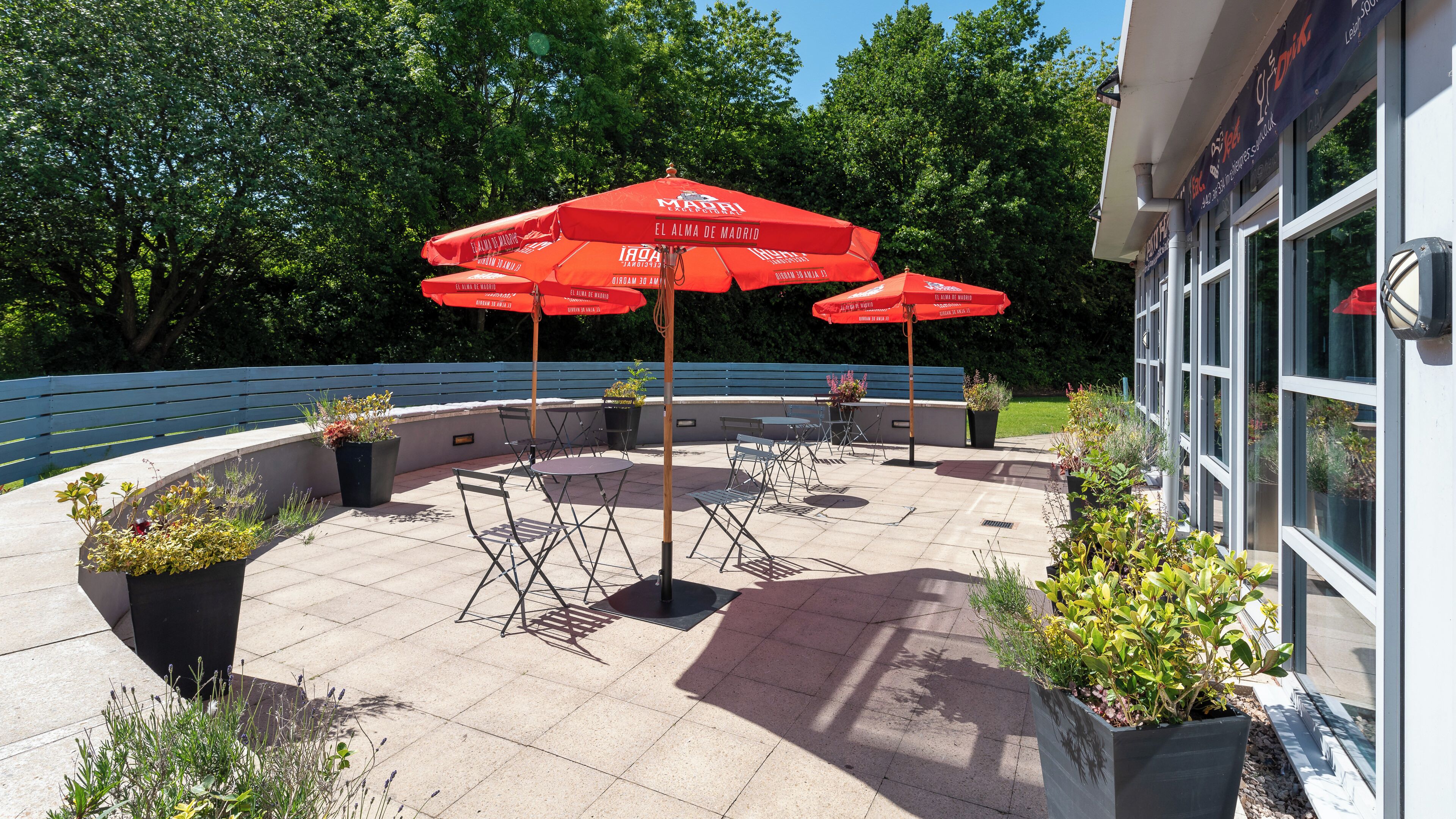 An outdoor patio area with red umbrellas, seating, and potted plants.