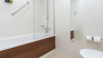 Un baño moderno con ducha envuelta en vidrio, tocador de madera y inodoro blanco.
