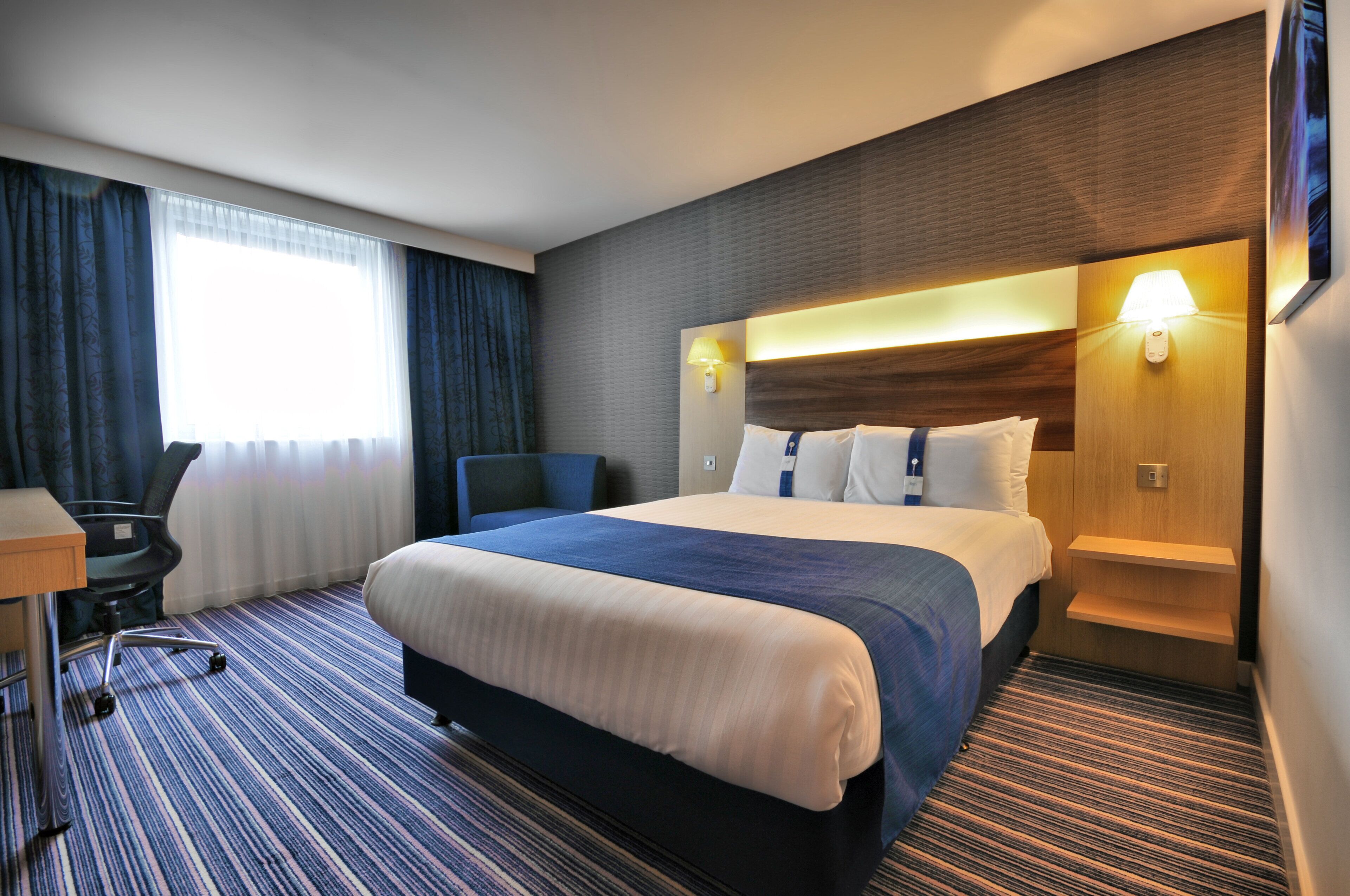 A hotel room with a bed, desk, chair, and a view of the outdoors.