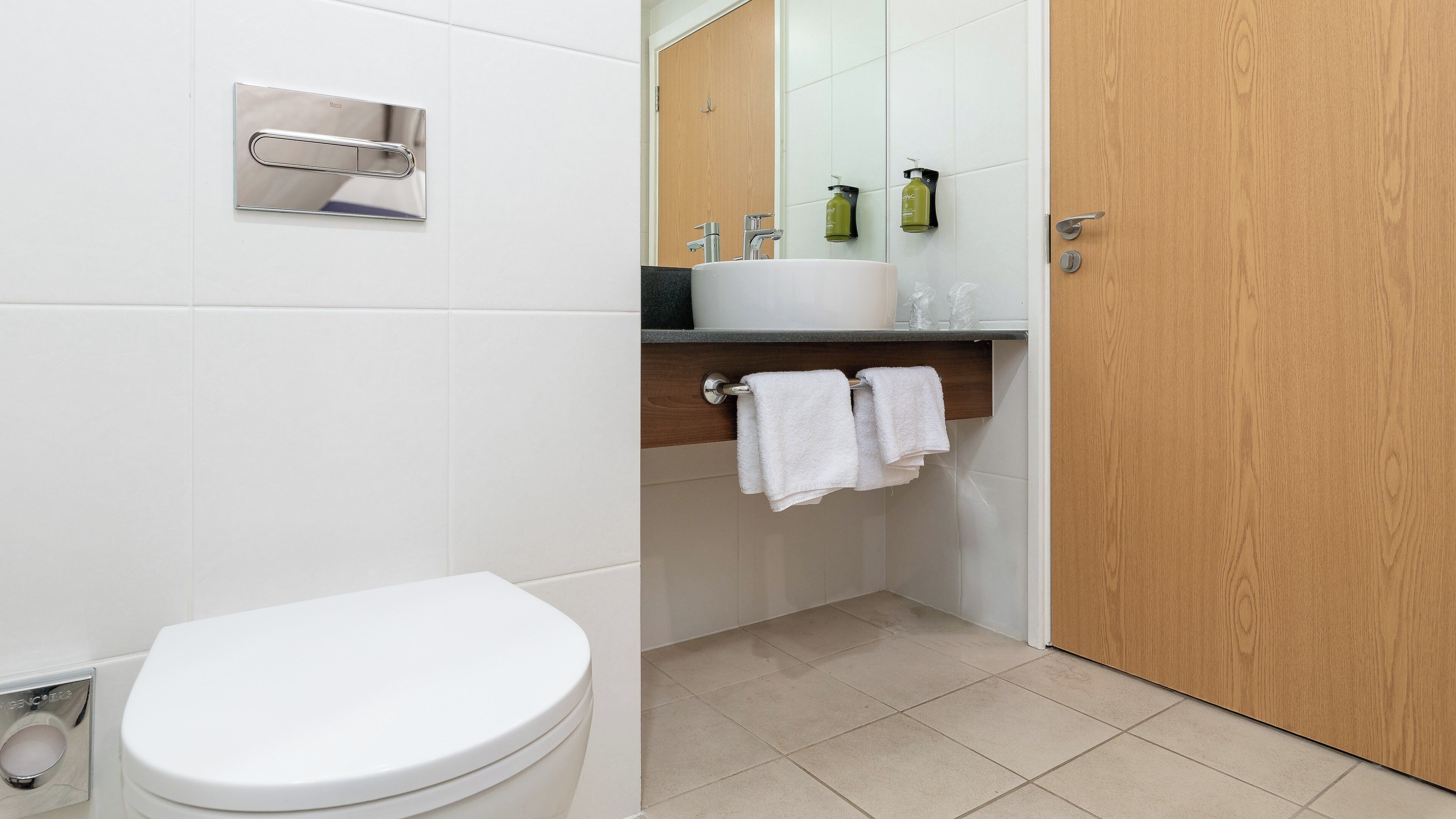 Un baño moderno con inodoro blanco, lavamanos con espejo y puerta de madera.