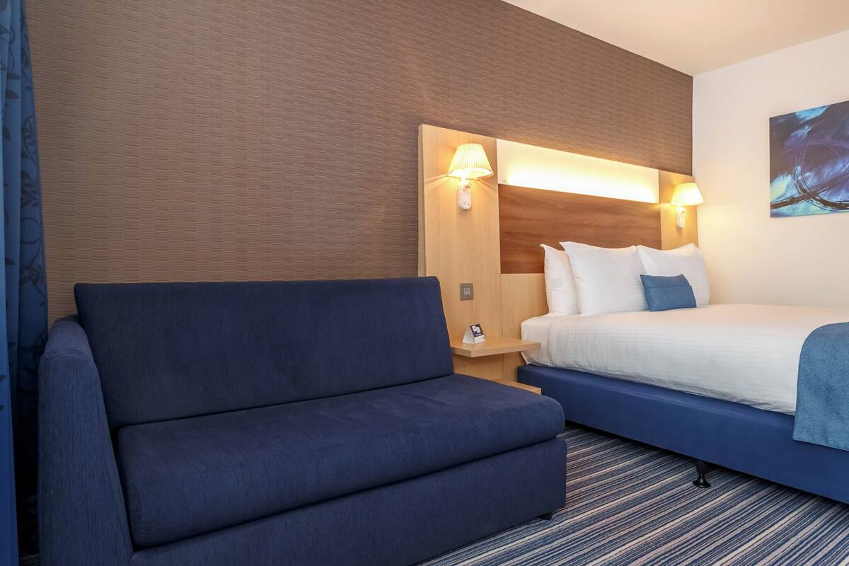 A hotel room with a blue sofa, a bed with white bedding, and a wooden headboard.