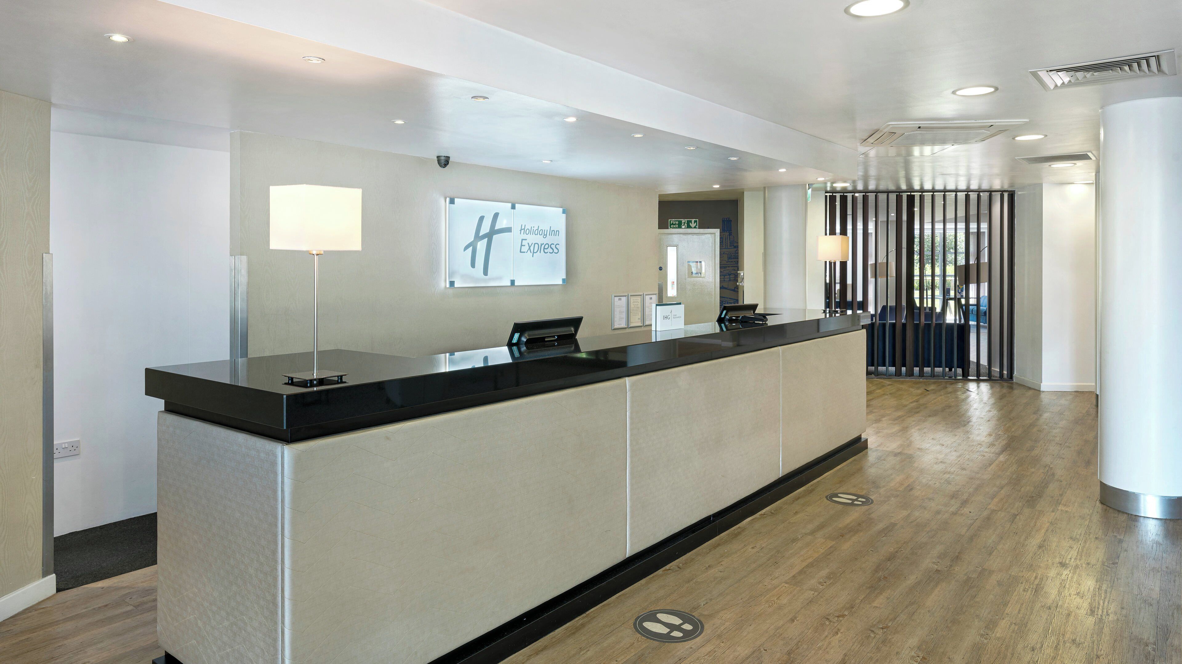 Ein moderner Hotelrezeptionstresen, ein Schild mit der Aufschrift Holiday Inn Express und Blick auf den Eingangsbereich.