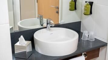 Un baño con un lavabo blanco, un espejo y una encimera negra. Hay dos jabones en la pared.