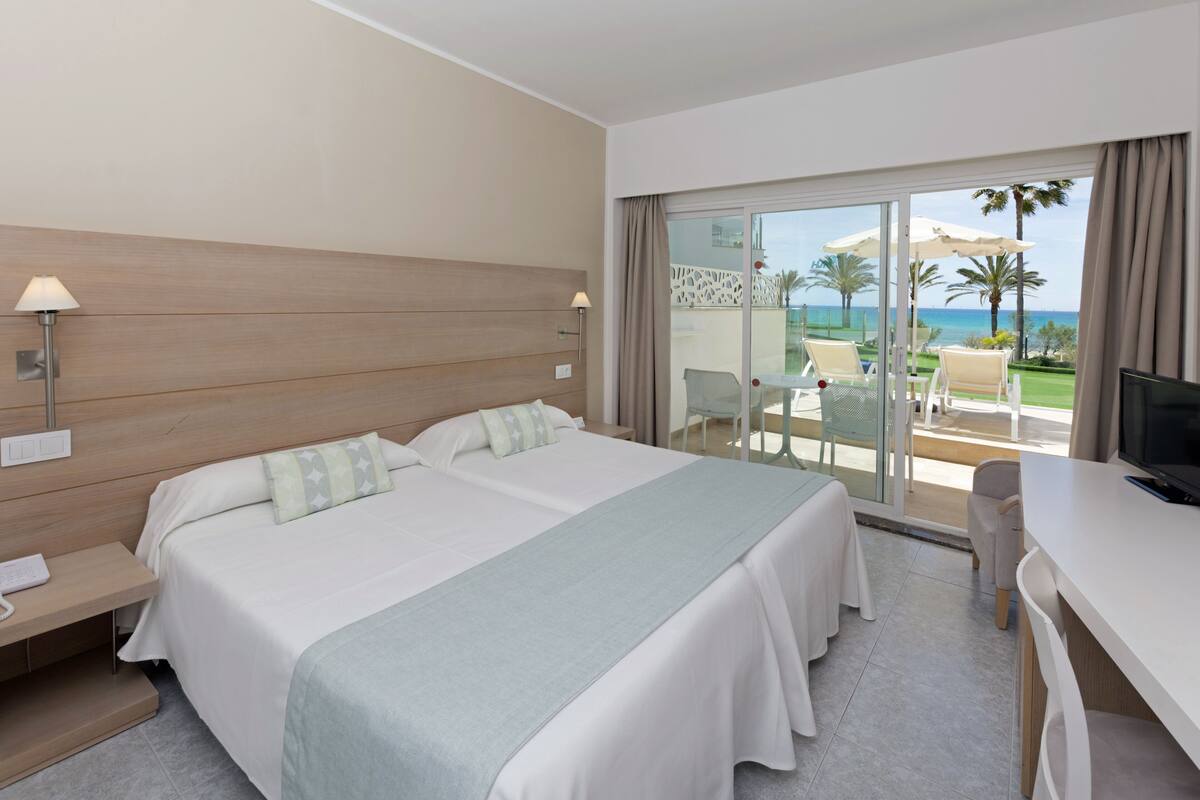 Een hotelkamer met een groot bed, een bureau en een balkon met uitzicht op zee.