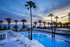 A poolside area with lounge chairs and umbrellas, palm trees, and a view of the ocean at sunset. - Hotel HSM Golden Playa (Palma de Mallorca)