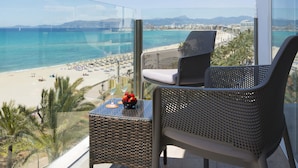 A balcony with wicker chairs, a small table, and a view of a beach and ocean. - Hotel HSM Golden Playa (Palma de Mallorca)