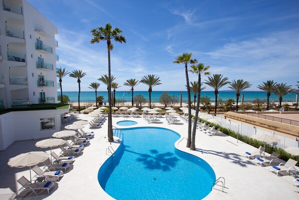 A pool area with lounge chairs and umbrellas, surrounded by palm trees and a view of the ocean. - Hotel HSM Golden Playa (Palma de Mallorca)