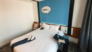 A hotel room with a bed, a nightstand, a wall with a blue accent, and a window with curtains.