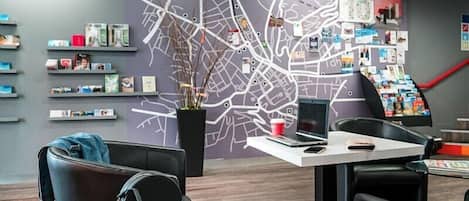 A modern office space with a large wall map, shelves with books and binders, and a desk with a laptop and a coffee cup.