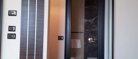 A hotel room with a bed, a bathroom with a toilet and sink, and a hallway with a door leading to the bathroom.