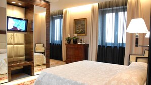 A hotel room with a bed, a chair, a desk, a television, a painting, and a lamp. - Hotel Excelsior (La Maddalena)