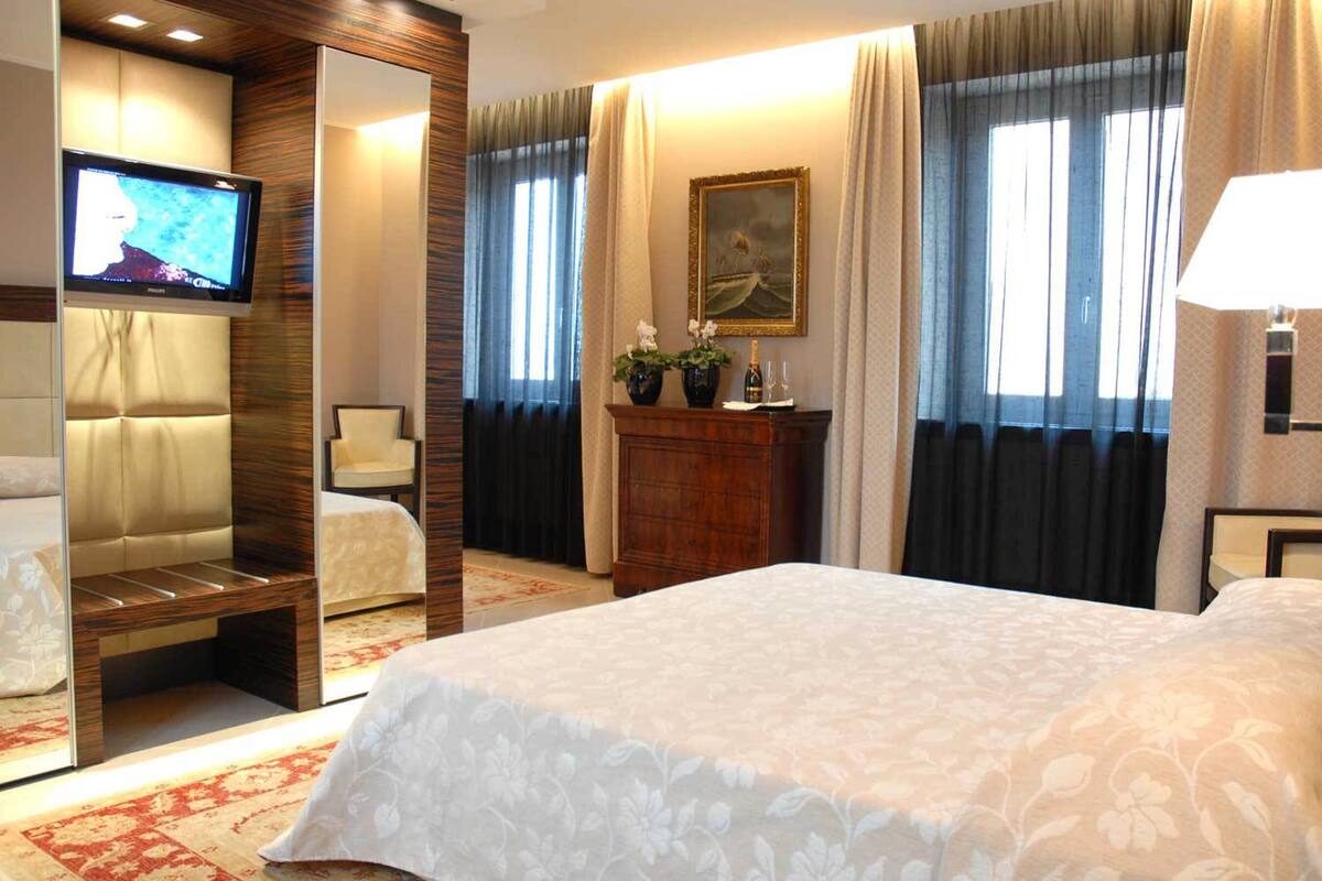 Una camera d'albergo con un letto, una sedia, una scrivania, una televisione, un quadro e una lampada.