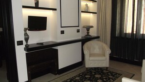 A modern living room with a dark wood console table, a white armchair, and a large mirror. - Hotel Excelsior (La Maddalena)
