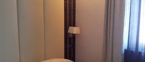 A hotel room with a bed, a nightstand, a lamp, and a window with curtains.