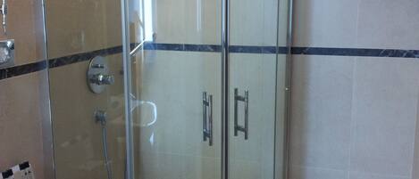 A modern bathroom with a glass-enclosed shower, a sink, and a small stool.