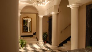 A grand hallway with checkered flooring, white columns, and a staircase leading to an upper level. - Hotel Excelsior (La Maddalena)